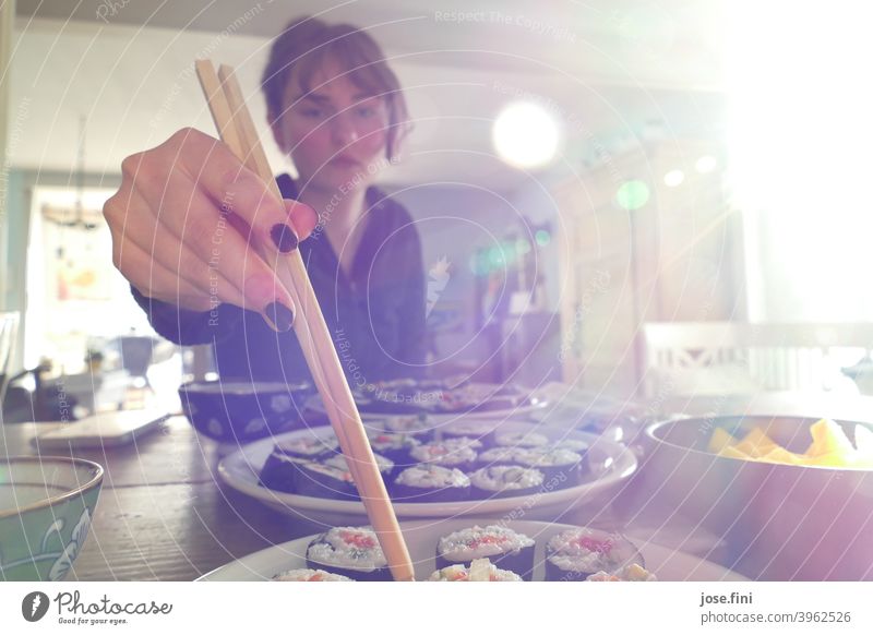 Junge Frau isst vegetarisches, selbstgemachtes Sushi, mit Stäbchen, Lichteinfall von rechts. Japanisch rollen Reis asiatisch traditionell Wasabi Ingwer