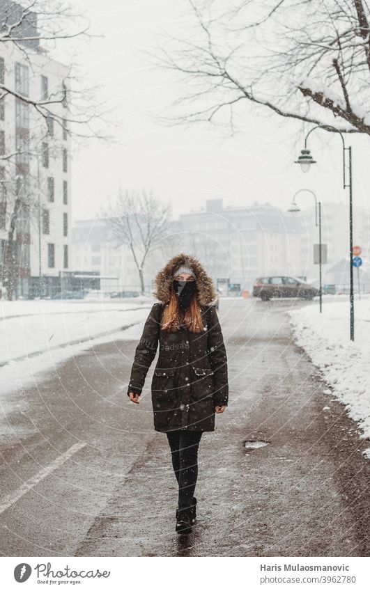 Frau mit Gesichtsmaske geht im Freien im Schnee Erwachsener allein attraktiv schön schwarz brünett kalt selbstbewusst Coronavirus covid-19 niedlich leer