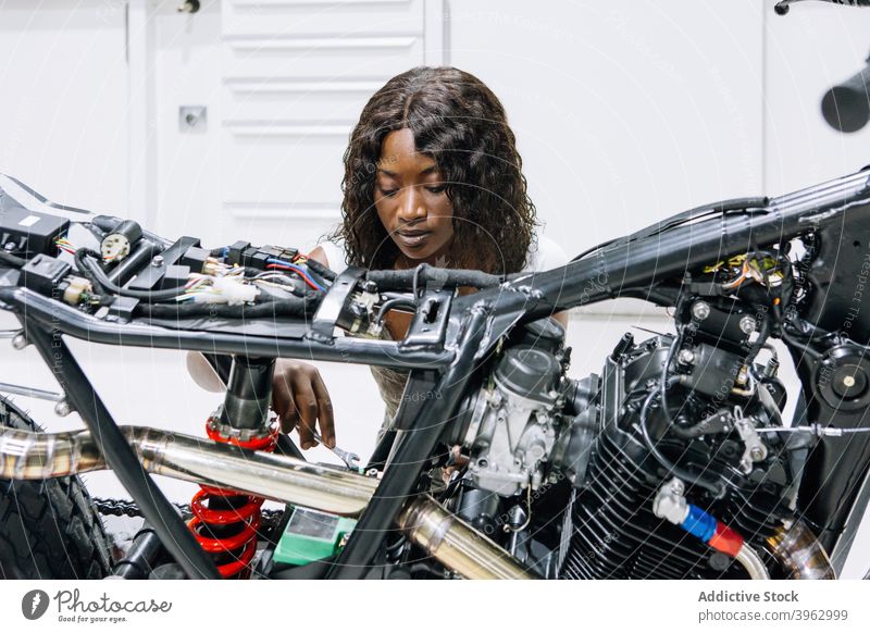 Schwarze Frau repariert Motorrad in Garage Mechaniker fixieren Werkstatt Reparatur Schraubenschlüssel Dienst ethnisch schwarz Afroamerikaner Arbeit Techniker