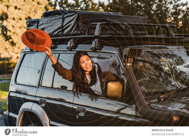 Entzückter ethnischer Reisender im Auto Frau PKW gucken Wellenhand heiter Automobil Fenster Urlaub Ausflug asiatisch Australien Autoreise ausdehnen Arme