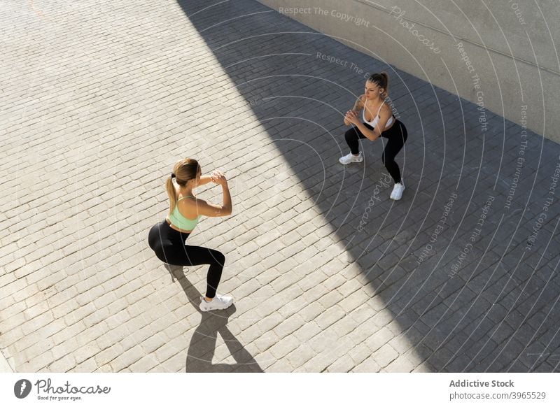 Sportlerinnen machen Kniebeugen beim Training in der Stadt Übung Zusammensein Athlet Großstadt Straße Schatten sonnig Frau üben Fitness Vitalität schlank