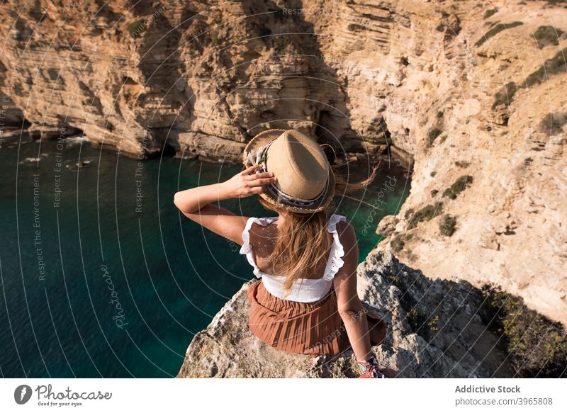 Anonyme Frau in Sommerkleidung sitzt in Klippe Küstenlinie felsig Berge u. Gebirge Feiertage mediterran Horizont bewundernd Seeküste jung Tourismus