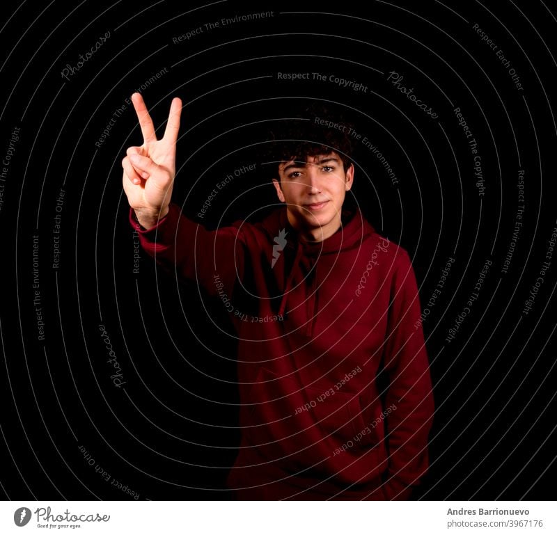 Attraktiver junger Mann macht das Siegessymbol auf einem schwarzen Studio Hintergrund Glück Kaukasier photogen gestikulieren Hemd schön positiv Erwachsener