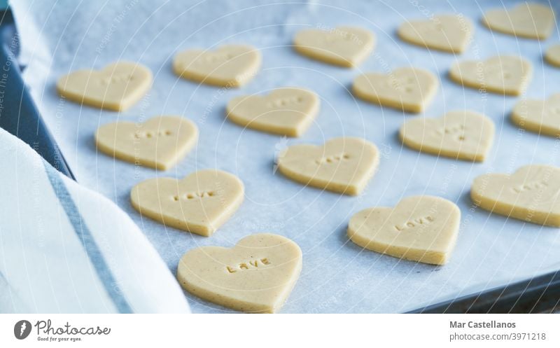 Herzförmige Kekse mit dem Wort LIEBE bereit zum Backen. Gebäck-Konzept. Valentinsgruß Geschenk heiter Datierung Cookies Valentinstag Liebe Briefe roh Backblech