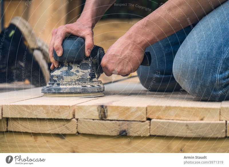 Nahaufnahme eines Arbeiters, der Holzbretter mit einer Schleifmaschine schleift Maschine Schleifen Bretter Knie Hand Arme arbeiten Staubwischen Werkzeug Gerät