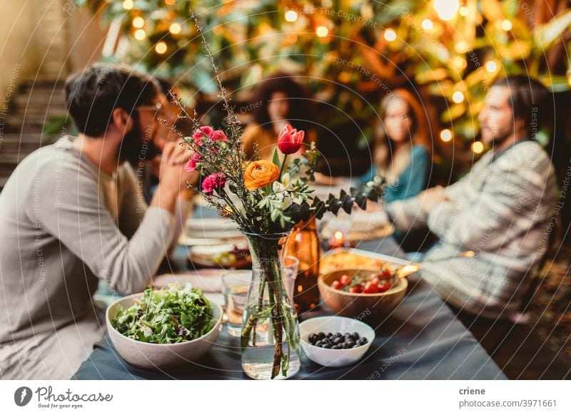 Freunde am Esstisch mit Blumen und Essen Erwachsener offen im Freien junger Erwachsener Alkohol Hinterhof zu feiern plaudernd Abendessen Dinnerparty Vielfalt