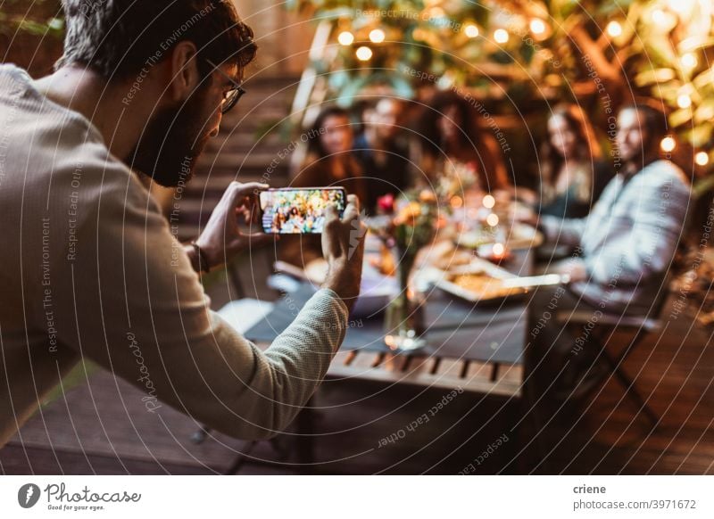 junger Erwachsener, der seine Freunde mit dem Telefon bei einer Dinnerparty fotografiert offen im Freien Smartphone Alkohol Hinterhof zu feiern plaudernd