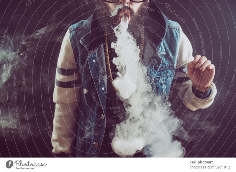 Junger Mann mit Bart, der eine Dampfwolke wirft. Schwarzer Hintergrund. Vaping eine elektronische Zigarette Raps vaping Rauch Erwachsener Cloud cool Lifestyle