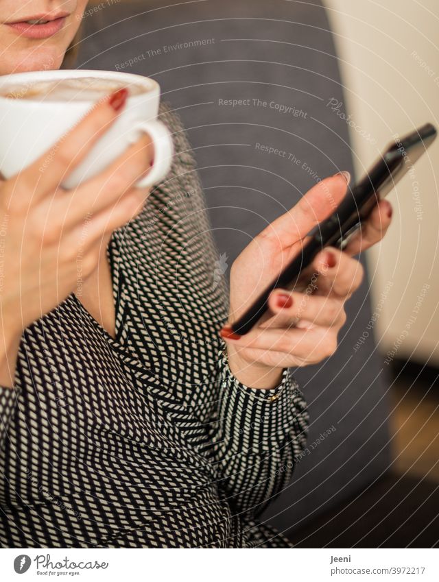 Junge hübsche Frau sitzt in einem Café, trinkt einen Cappuccino und blickt auf ihr Smartphone Blick E-Mail Telefon Surfen Internet Hand Hände Fingernagel