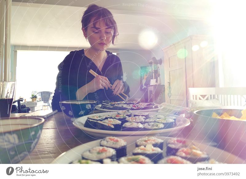 Junge Frau sitzt mit Essstäbchen an einem Tisch mit Sushi. junger Erwachsener Teenager Schüler Lifestyle Person selbstgemacht Lebensmittel Food-Fotografie