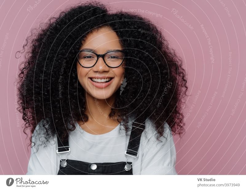 Close up Porträt der dunkelhäutigen Frau mit knackigen Haaren, lächelt glücklich, trägt eine optische Brille, lässige Kleidung, posiert über lila Hintergrund drückt gute Gefühle. Afroamerikanischer Student posiert innen