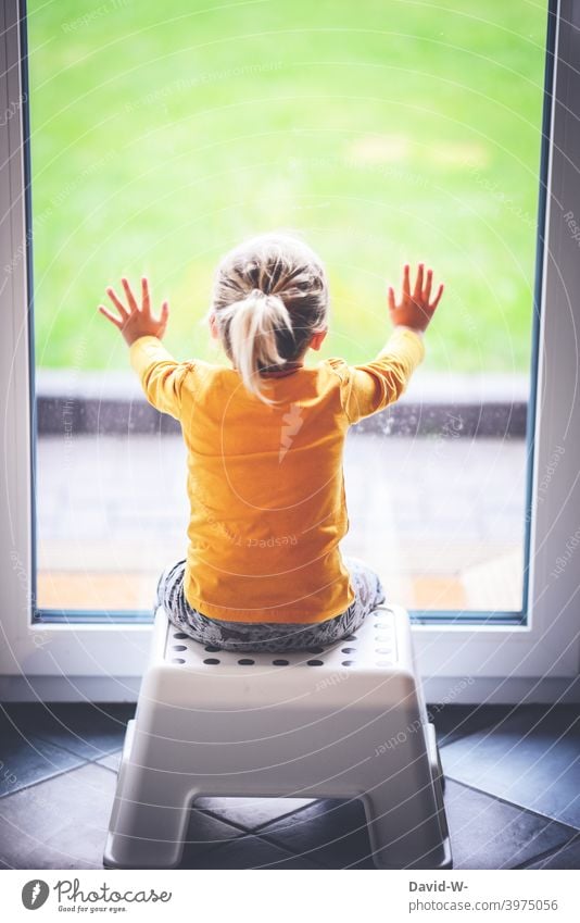 kleines Kind sitzt vor einem verschlossenen Fenster und schaut