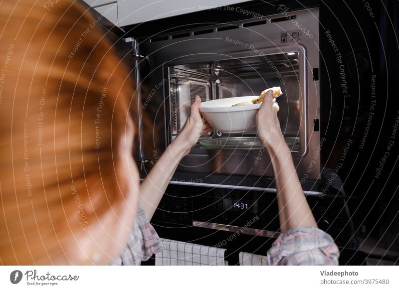Frau erwärmt Essen in der Mikrowelle. In Möbel eingebaute Küchengeräte. Lebensmittel Ofen Heizung Kulisse Zeitschaltuhr Essen zubereiten Koch heimwärts
