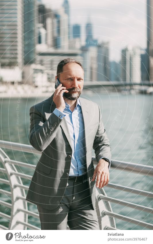 Junger Geschäftsmann mit einem Telefon in den Händen, stehend in einer großen Stadt zwischen Hochhäusern Büro Mann Smartphone modern gelungen Großstadt Anzug