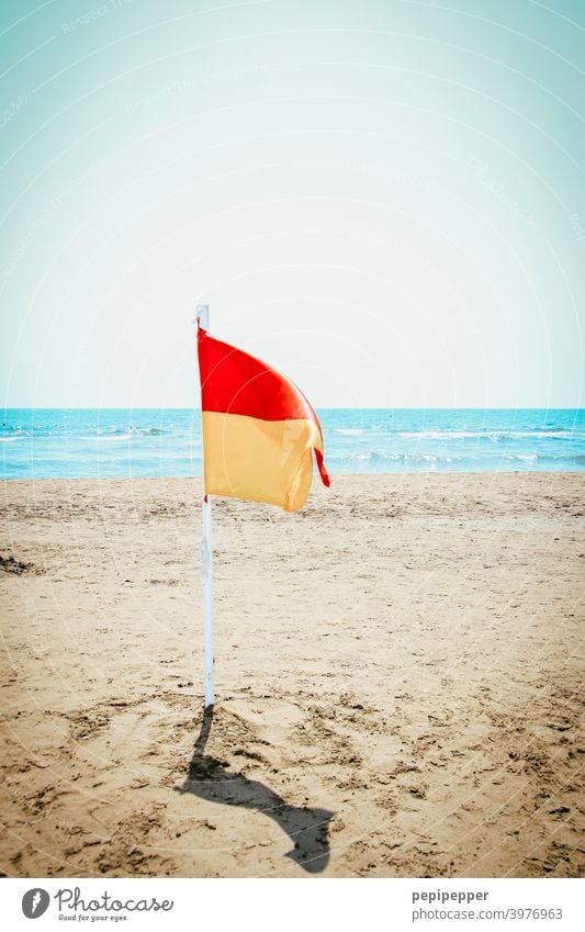 einsame Flagge am leere Strand Fahne rot Wind Fahnenmast blau Menschenleer gelb flattern wehen Himmel Außenaufnahme Wolken Strandspaziergang Sand Meer Wasser