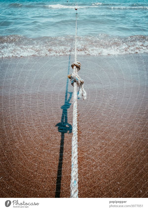 ein gespanntes Seil am Strand das ein Boot festhält maritim Wasserfahrzeug Tau Außenaufnahme Befestigung Küste Nahaufnahme Knoten Knotenpunkt festhalten