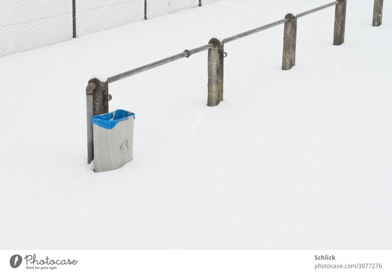 Mülleimer mit blauer Plastiktüte am Rande eines Sportplatzes vom hohen Schnee und dem Coronavirus vor lästigen Benutzern geschützt Zaun Schneefläche