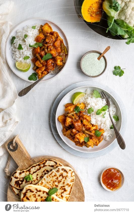 Draufsicht auf ein vegetarisches, veganes indisches Balti-Curry mit Blumenkohl und Kürbis, serviert mit Raita, Naan-Brot und Mango-Chutney und Reis auf einem weißen Hintergrund