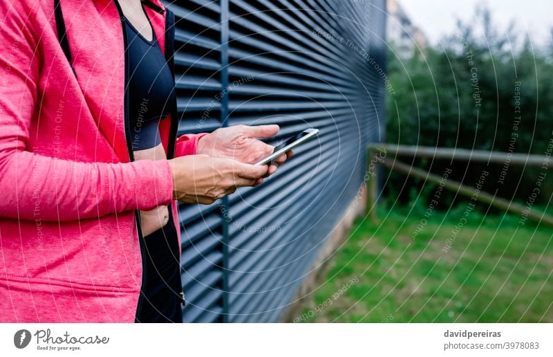 Unerkennbare Sportlerin mit Mobiltelefon unkenntlich Frau Athlet Mittelteil Gitterrost-Hintergrund Handy Profil Perspektive Porträt Körper Fitness Hände