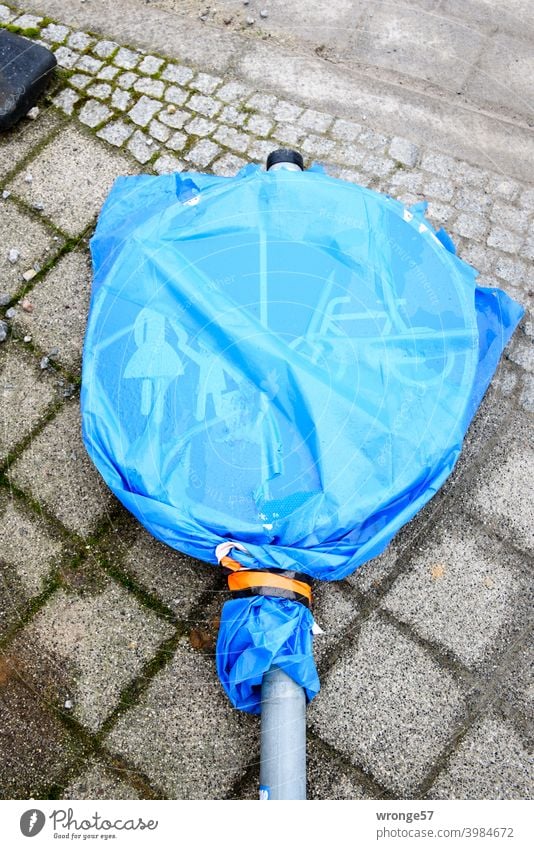 Ein mit einem blauen transparenten Müllsack verhülltes Verkehrszeichen (Verkehrsschild Nr. 241-31) liegt auf grauem Kopfsteinpflaster Fuß- und Radweg