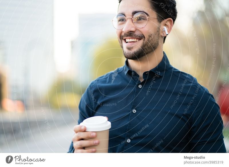 Junger Mann hält eine Tasse Kaffee, während er im Freien spazieren geht. Porträt jung urban wegnehmen abschließen Getränk Nahaufnahme Ohrhörer Freizeit