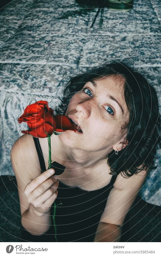 Porträt von blauäugigen schönen Mädchen beißen ein Blütenblatt einer roten Rose sinnlich Frau Dame Teenager Jugend jung hübsch Augenkontakt