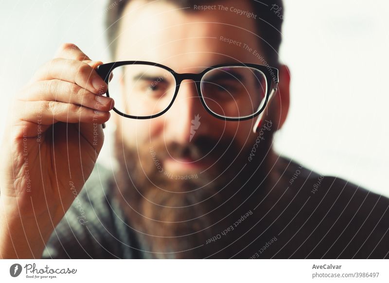 Ein unscharfes Hipster-Männchen, das eine Blaulichtbrille im Fokus der Kamera hält, während es lächelt 20s Kontemplation Unternehmer genial