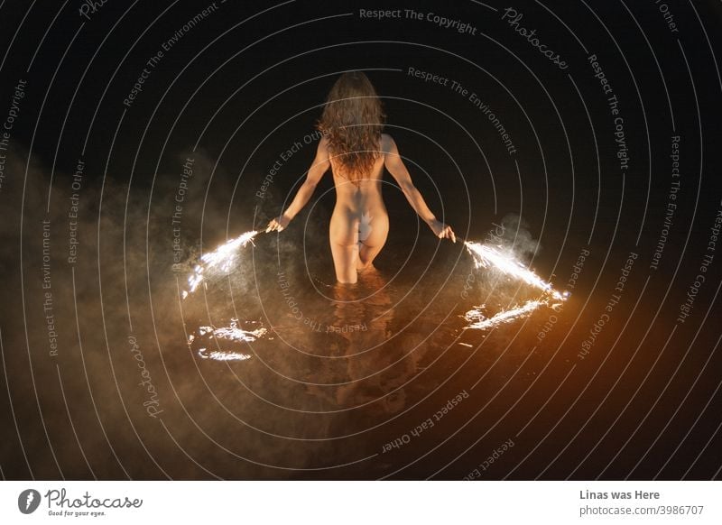 Wildes und nacktes Mädchen schwimmt in der Nacht. Erotisches Bild von einem brünetten Modell. Feuerwerk in ihren Händen, sexy Rücken zeigen ihre perfekten Kurven, Rauch, und dunkles Wasser macht diese Szene stimmungsvoll und sinnlich.