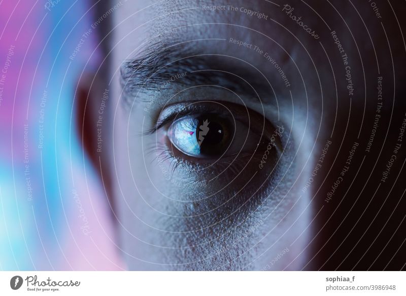 Ausdrucksstarker Blick - Nahaufnahme eines Auges mit unscharfem blauem und rosa Neonlicht-Hintergrund und hohem Kontrast Disco-Licht hoher Kontrast Mann Farbe
