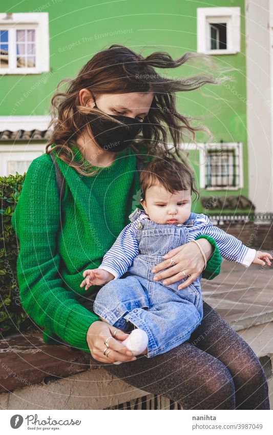 Bild in Grüntönen einer jungen alleinerziehenden Mutter mit ihrem Baby während der Covid-Pandemie COVID Coronavirus Familie Mutterschaft Mama Mundschutz