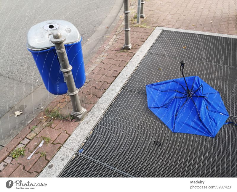 Blauer Müllheime neben und blauer Regenschirm auf dem Lüftungsgitter einer U-Bahn Station an der Senckenberganlage im Westend von Frankfurt am Main in Hessen