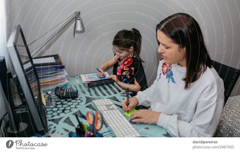 Frau bei Telearbeit mit ihrer Tochter beim Zeichnen Vereinbarkeit von Familienarbeit Heimarbeit Coronavirus Quarantäne Schreiben einer Notiz Computer Seuche