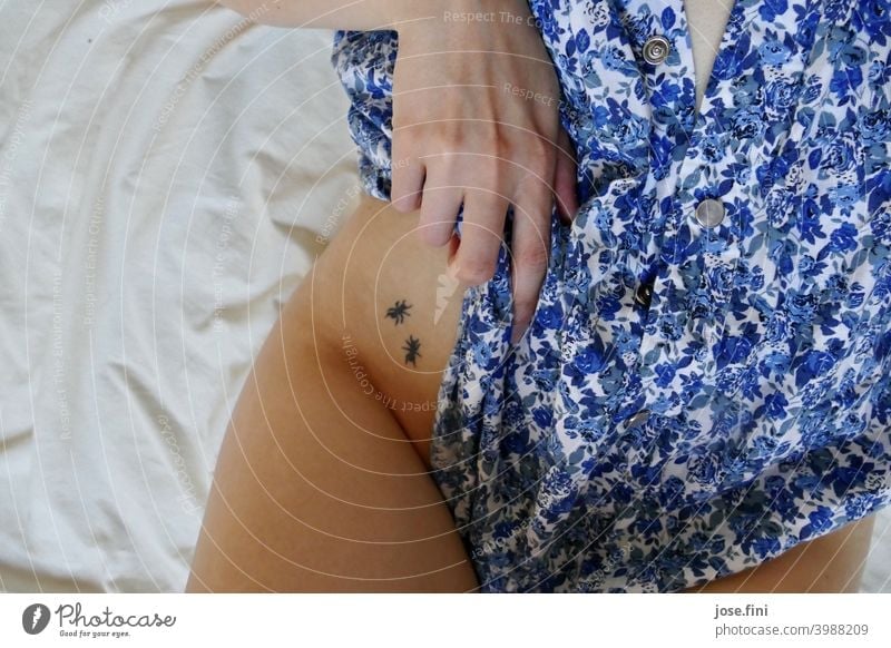 mittlerer Körperausschnitt einer Frau in Blümchen Bluse, tätowiert an der Hüfte natürliches Licht Ameisen Junge Frau schön feminin Schlank Bett Laken dünn