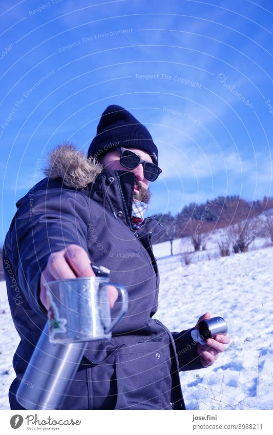 Das Tee-einschenk Model, Junger Mann mit Sonnenbrille im Schnee, Teekanne und Becher in der Hand. Lifestyle Freizeit & Hobby im Freien Wandertag Landschaft