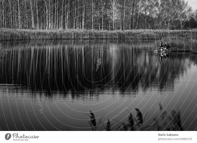 zwei Fischer in einem Boot mit Spiegelung in einem stillen Flusswasser bei Dämmerung auf Herbstlandschaft. allein Anker schön Lettland Liegeplatz Birke