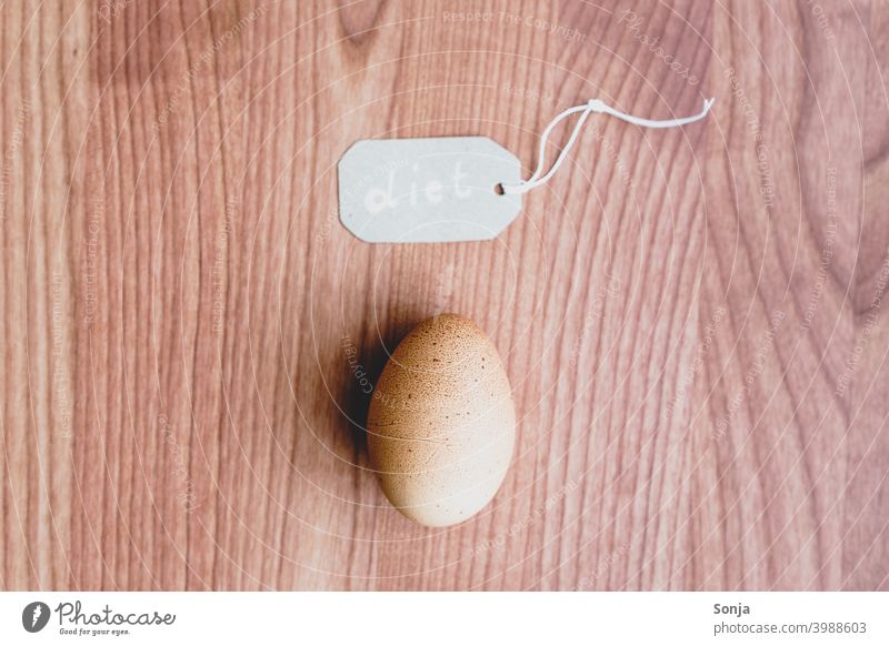 Ein braunes Ei und ein Etikett mit dem Wort diet auf einem Holztisch einzeln Protein eiweißreich Eiweißquelle frisch organisch Lebensmittel Gesundheit Frühstück