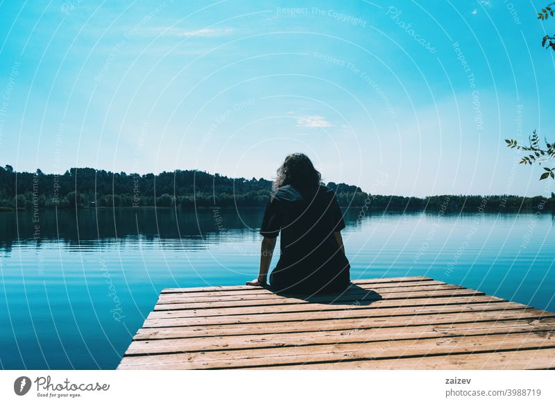 Mädchen sitzt auf dem Rand des Banyoles See mit der Landschaft im Wasser reflektiert Harmonie Meditation entspannend horizontal Profil Ruhe Person nachdenken