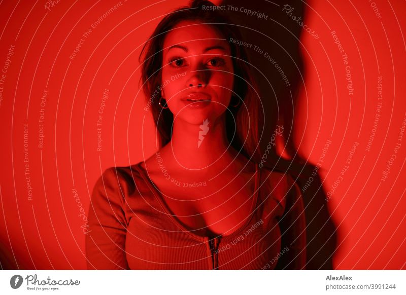 Porträt einer jungen Frau in einem Raum mit rotem Licht - das ganze Bild ist rot Junge Frau hübsch brünett langhaarig schlank feminin Teenager 18-25 Jahre