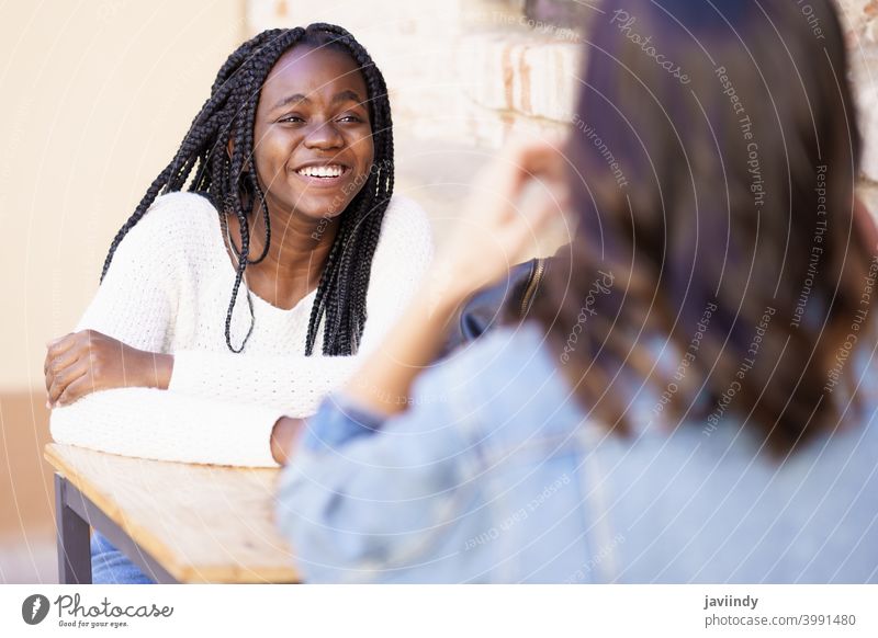 Zwei multiethnische Freunde unterhalten sich an einem Tisch vor einer Bar. Frau im Freien rassenübergreifend Fröhlichkeit Mädchen Freundschaft Glück Lächeln