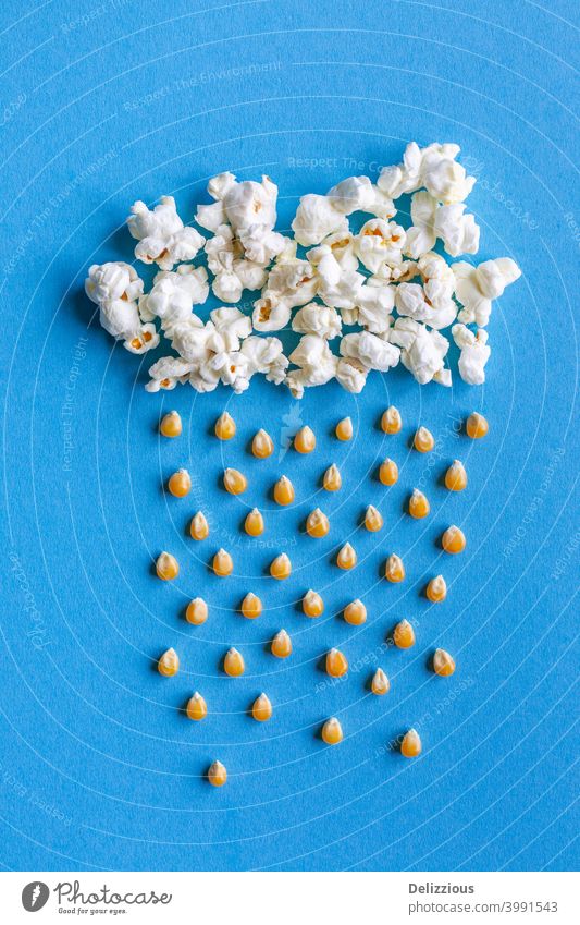 Große Popcorn-Wolke mit Regen aus Maiskörnern auf blauem Hintergrund Kinofilm Himmel Popkorn kreativ Cloud Lebensmittel gelb Snack Kunst weiß geschmackvoll