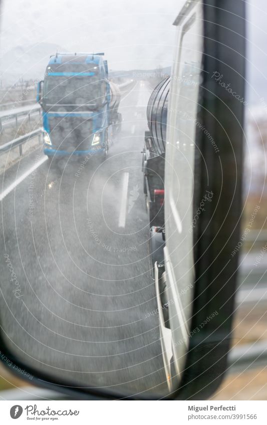 Rückspiegel eines LKWs an einem regnerischen Tag mit der verschwommenen Sicht eines anderen vorbeifahrenden LKWs. Lastwagen Verkehr Rückansicht Überholen Seite