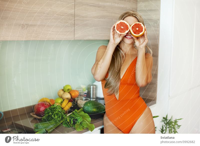 Porträt eines sportlichen Mädchens mit einer Grapefruit in ihren Händen in der Küche mit frischem Gemüse und Obst. Das Konzept eines gesunden Lebensstils, Gesundheit, Schönheit