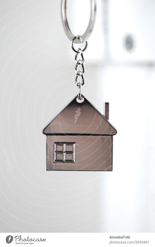 Silberner Hausschlüssel in weißer Tür, mit kleinem Schlüsselanhänger Haus, öffnende Tür zu neuem Haus, Heim, Investition, Immobilienkonzept, Platz für Text
