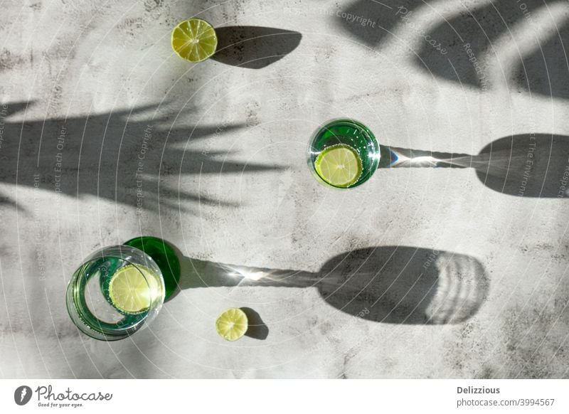Draufsicht auf Getränke und Schatten mit Limette, tropische Stimmung auf heller Fläche Wasser Bestandteil weiß Hintergrund Zitrusfrüchte Nahaufnahme Cocktail