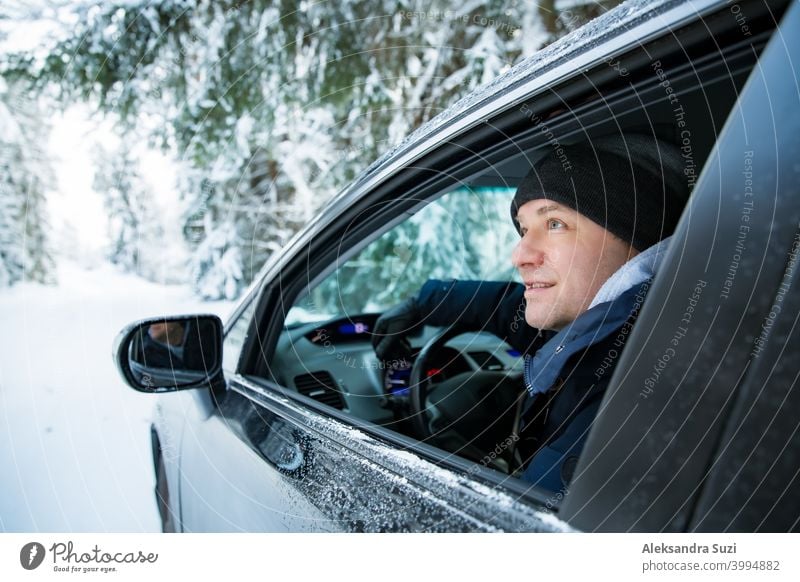 Mann in warmer Winterkleidung sitzt im Auto. Snowy Winter Landstraße, Auto mit Eis bedeckt, Schöne Wald unter dem Schnee. Schneesturm PKW kalt Arbeitsweg