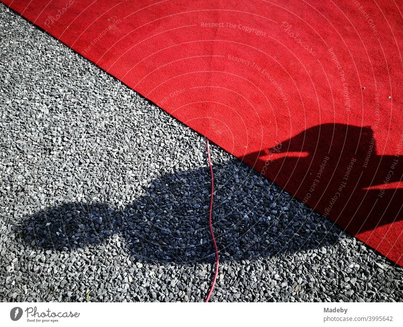 Schatten einer Frau mit Handtasche auf rotem Teppich und grauen Kieselsteinen bei einer Vernissage in Oelde bei Warendorf in Westfalen Roter Teppich Knallrot