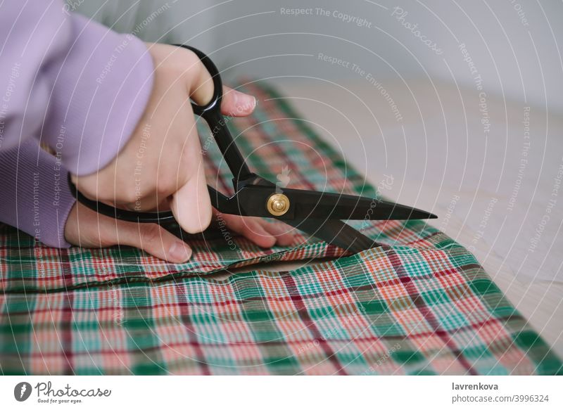 Nahaufnahme von Frau Hände halten Schere und Schneiden karierten Stoff für das Nähen Kleidung Näherin Gewebe Textil ausschneidend Beruf Schneider Werkstatt
