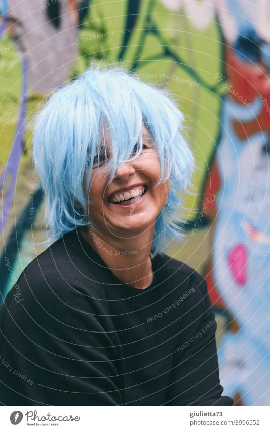 Porträt einer fröhlich, lachenden Frau / Künstlerin mit blauen Haaren Blick in die Kamera Vorderansicht Oberkörper Zentralperspektive Schwache Tiefenschärfe
