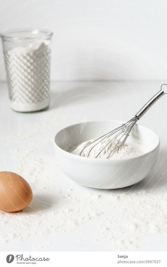 Mehl in einer Schüssel und ein Ei auf einem weißen Küchentisch backen Tisch Vorbereitung Frühstück weißer Hintergrund Nahaufnahme Teig Zutaten roh