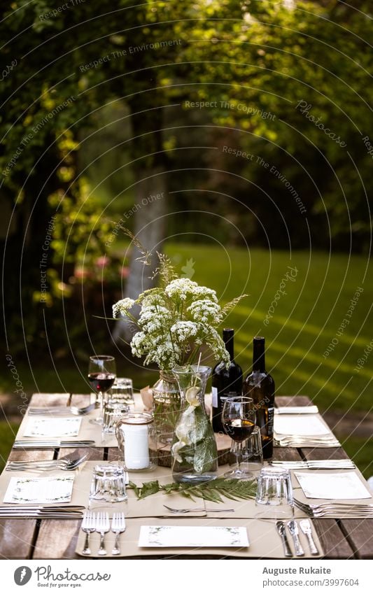 Servierter Restauranttisch im Freien Speisetafel Tisch Wein Weinglas Weinprobe Gießkanne Wasser Gabel Messer Glas Glasflasche Blumen und Pflanzen Sonnenlicht